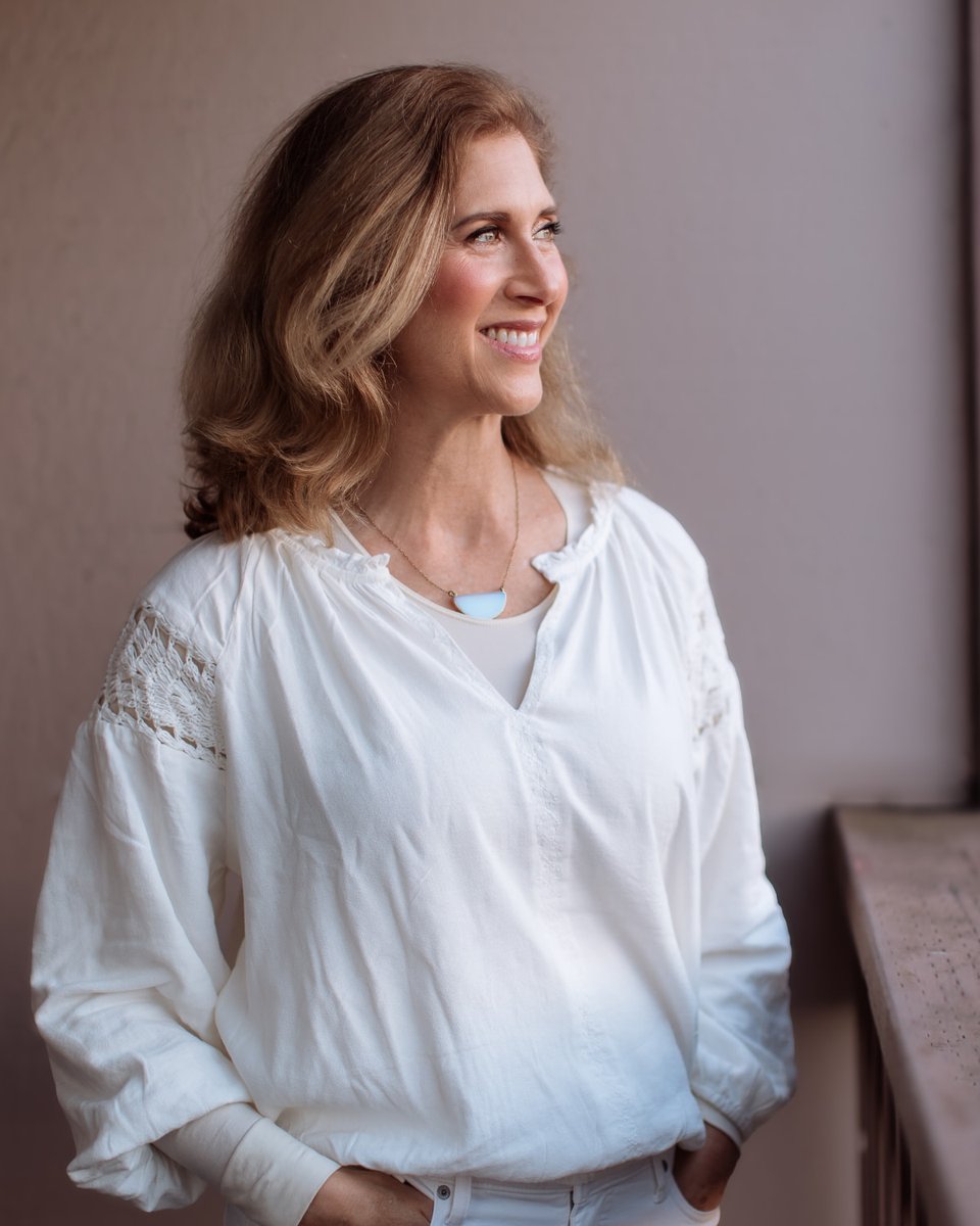 Sheira Kahn, licensed therapist, smiling by a window in a white blouse